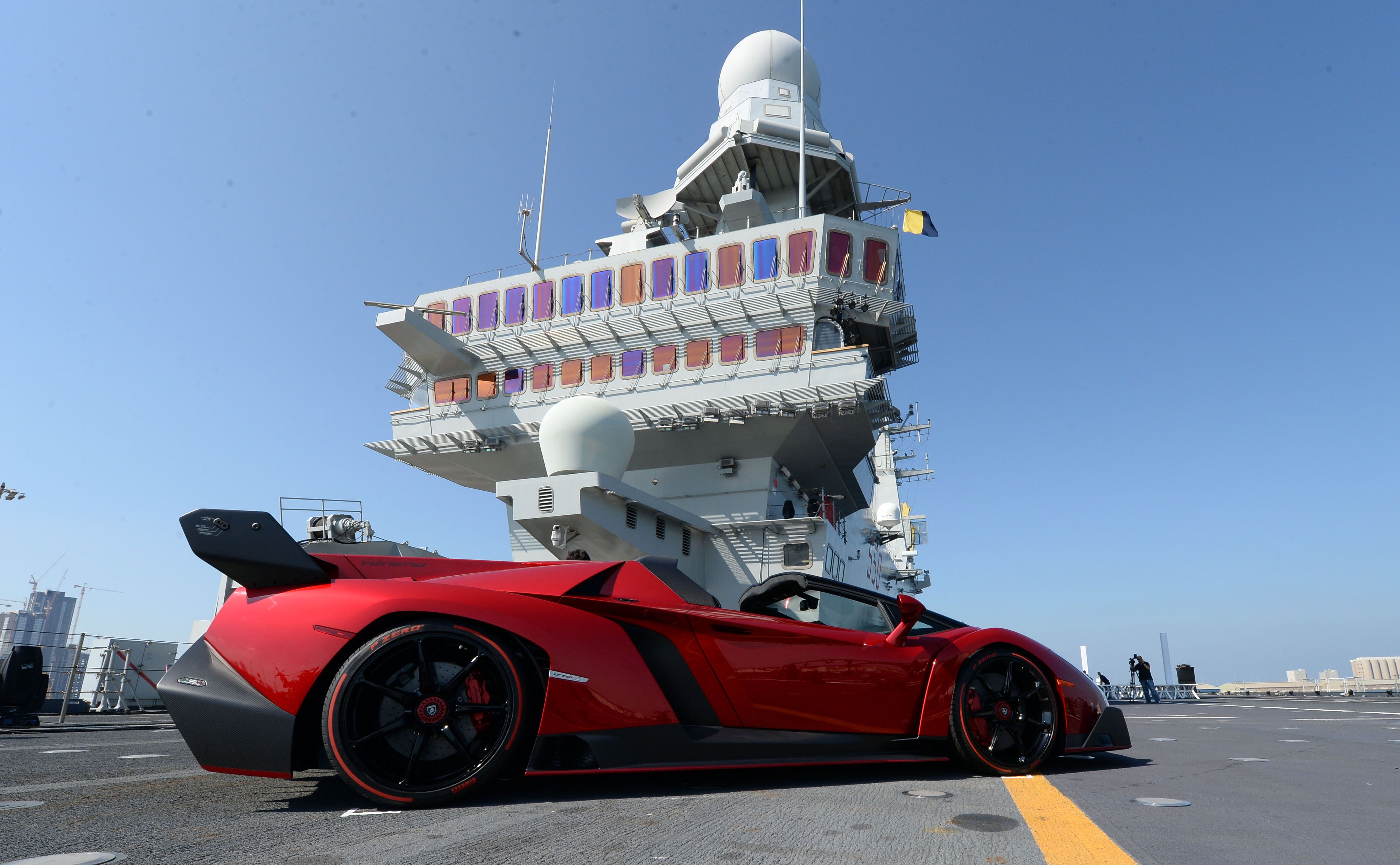 A red Lamborghini Veneno with black highlights, facing right on the deck of the Cavour ship.